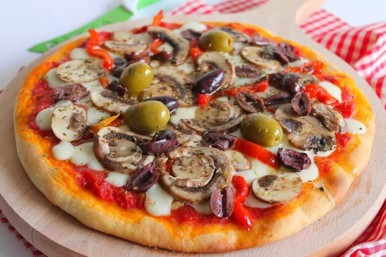 Pizza ai funghi e olive con formaggio fuso e salsa di pomodoro su tagliere di legno.
