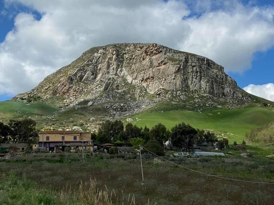 Un altopiano roccioso si erge sopra verdi colline e un piccolo insediamento rurale sotto un cielo nuvoloso.