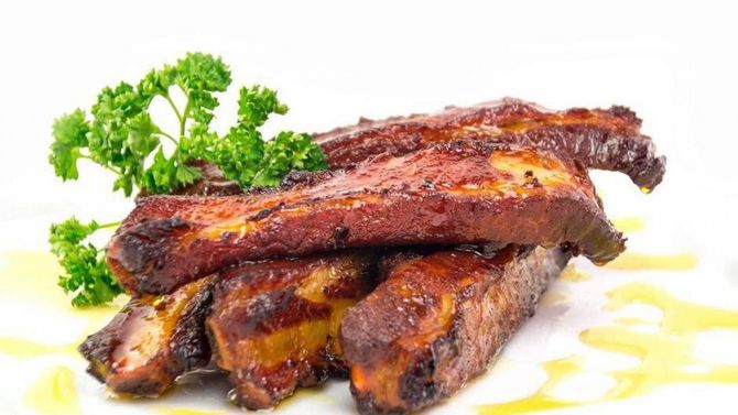 Costine grigliate glassate con salsa, guarnite con prezzemolo e servite su un piatto bianco.