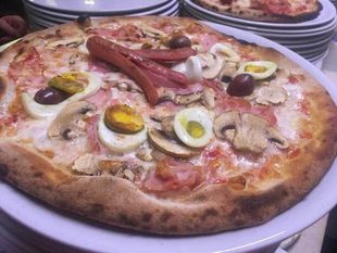 Pizza condita con uova, olive e carne su un piatto bianco a un tavolo di ristorante.