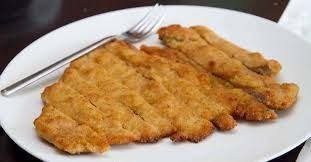 Cotoletta impanata dorata su un piatto bianco con forchetta
