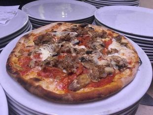 Due pizze su piatti bianchi, una condita con funghi e carne, su un tavolo apparecchiato