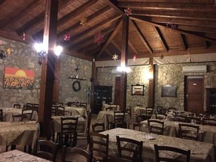 Sala da pranzo rustica in pietra con travi in legno, tavoli con sedie e calda illuminazione soffusa.