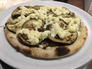 Pizza su pane piatto con formaggio fuso e funghi, servita su un piatto bianco.
