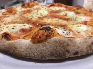 Primo piano di una pizza al formaggio con crosta dorata ed erbe aromatiche su un piatto bianco.