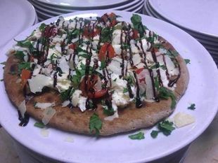 Pizza su pane piatto, farcita con formaggio, pomodori, verdure e salsa, servita su un piatto bianco.
