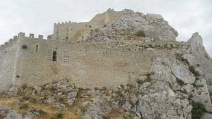 Rovine di una fortezza di pietra su una collina rocciosa sotto un cielo nuvoloso.