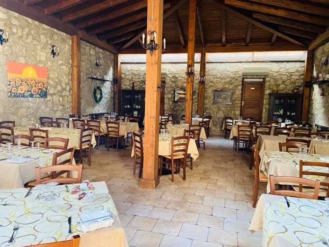 Sala da pranzo rustica di un ristorante in pietra con travi in ​​legno, tavoli a scacchi e sedie vuote.