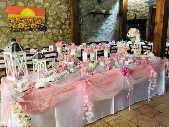 Tavolo dei dolci decorato in rosa con lanterne e dettagli floreali in uno spazio eventi con pareti in pietra.