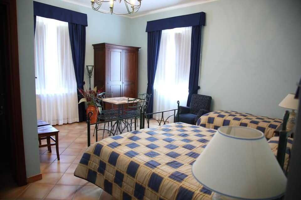 Camera da letto con due letti singoli, tende scure, mobili in legno e un piccolo tavolo da pranzo accanto a finestre luminose.