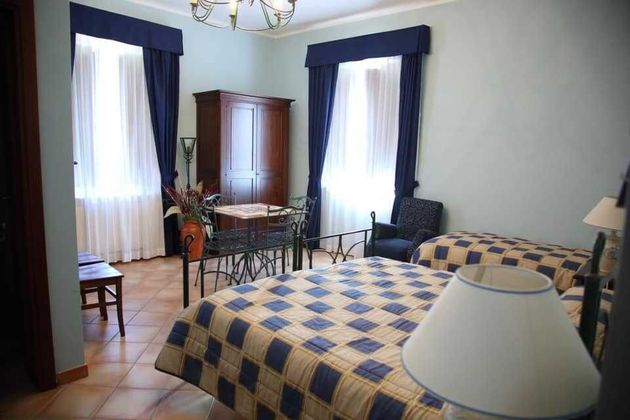 Camera d'albergo con due letti singoli, lenzuola a quadri blu, tende scure, scrivania, sedie e ampie finestre.