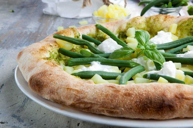 Pizza condita con fagiolini, cipolle e basilico su un piatto bianco