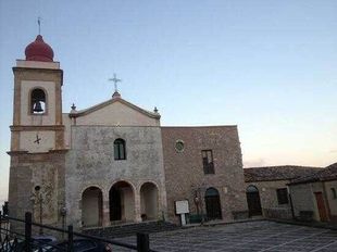 Chiesa in pietra con campanile dalla cupola rossa al crepuscolo, vista da un cortile.