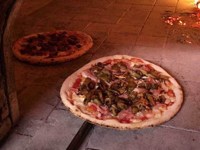 Due pizze in cottura in un forno a legna, una davanti e una dietro.