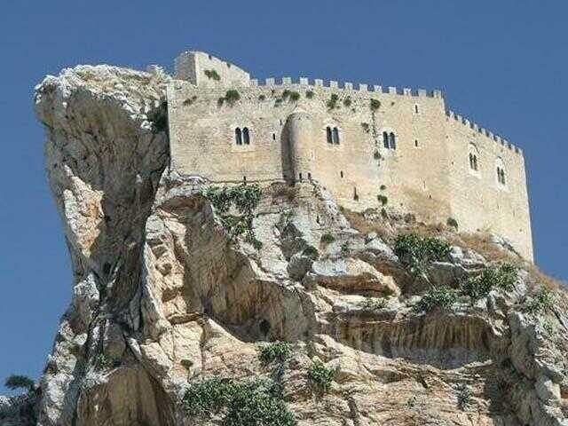 Fortezza di pietra incastonata in una scogliera rocciosa sotto un cielo azzurro