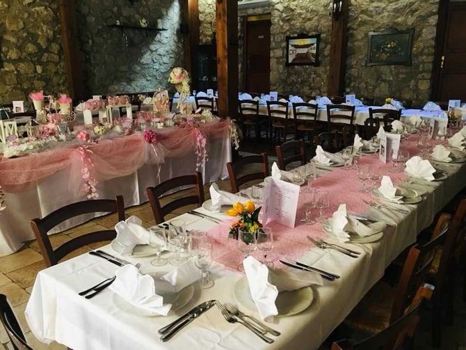 Elegante sala per banchetti con lunghi tavoli apparecchiati per un evento formale, decorata nei toni del bianco, del rosa e del nero.