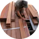 A man is measuring a piece of wood on a deck.