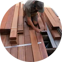 A man is measuring a piece of wood on a deck.