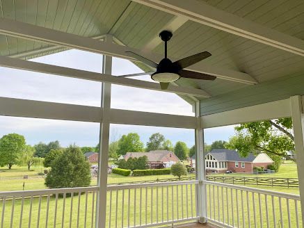 A screened in porch with a ceiling fan and a view of a field.