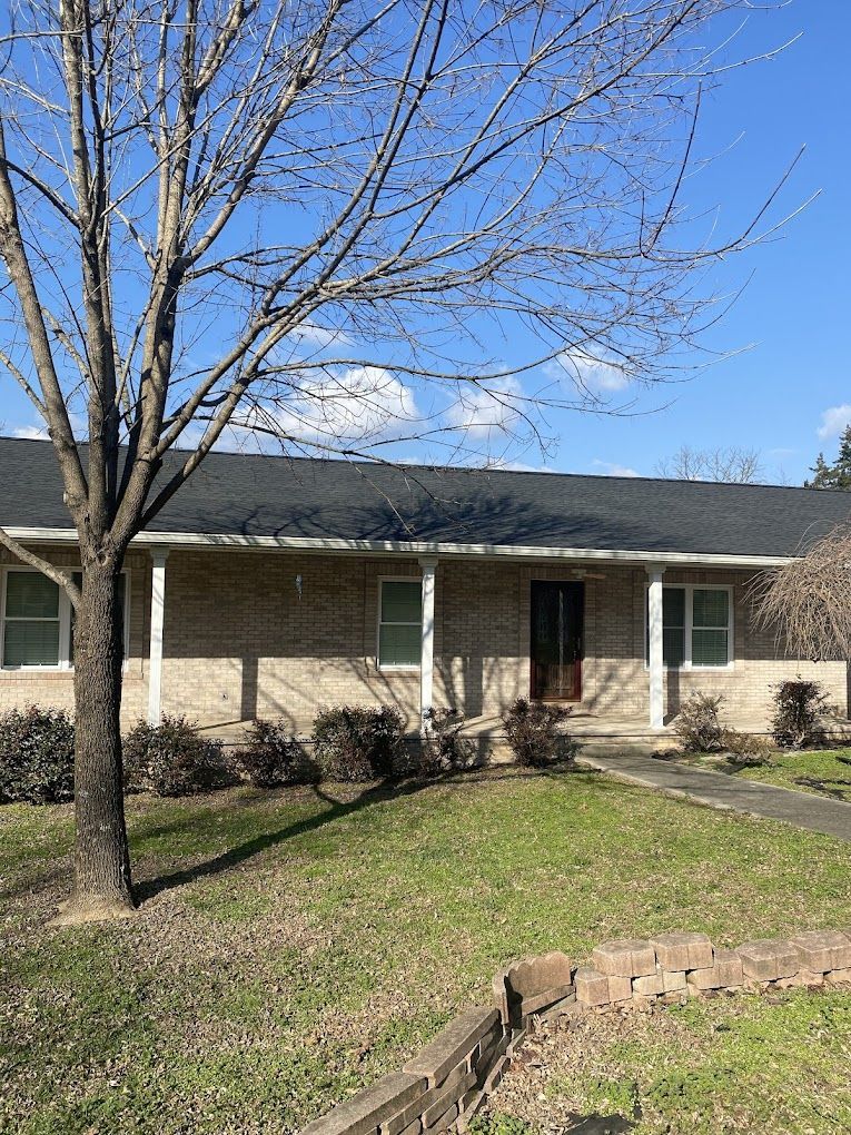 A house with a porch and a tree in front of it on a sunny day.