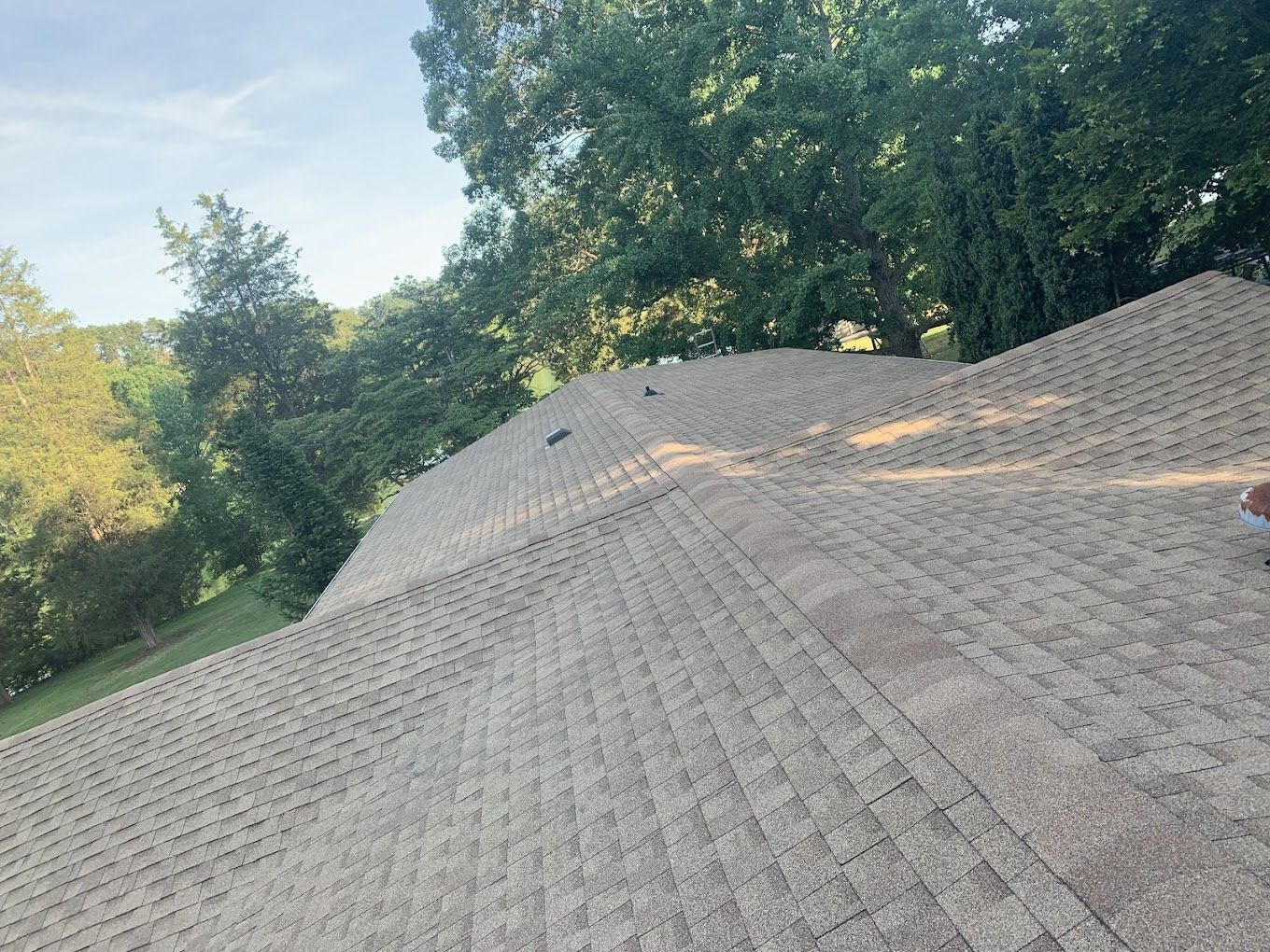 A roof with a lot of shingles on it and a green field in the background.