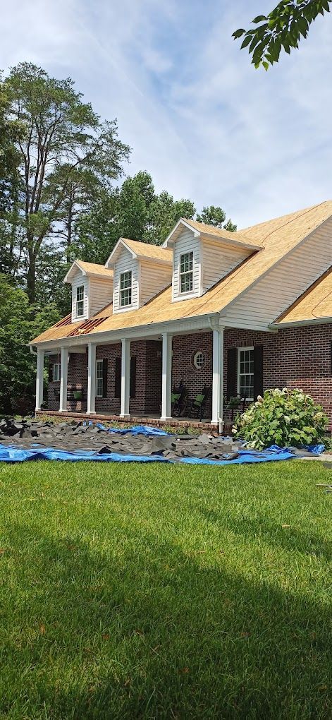 A large brick house with a porch and a roof that is being installed.
