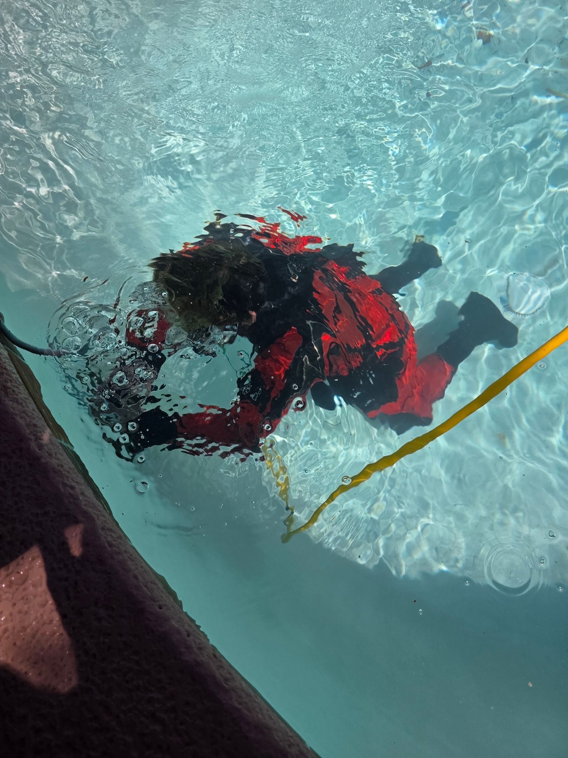 Person in red jacket and black boots swimming underwater beside a yellow rope.