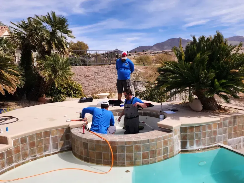 Three people working around a tiled backyard pool with desert landscaping and mountains in the background