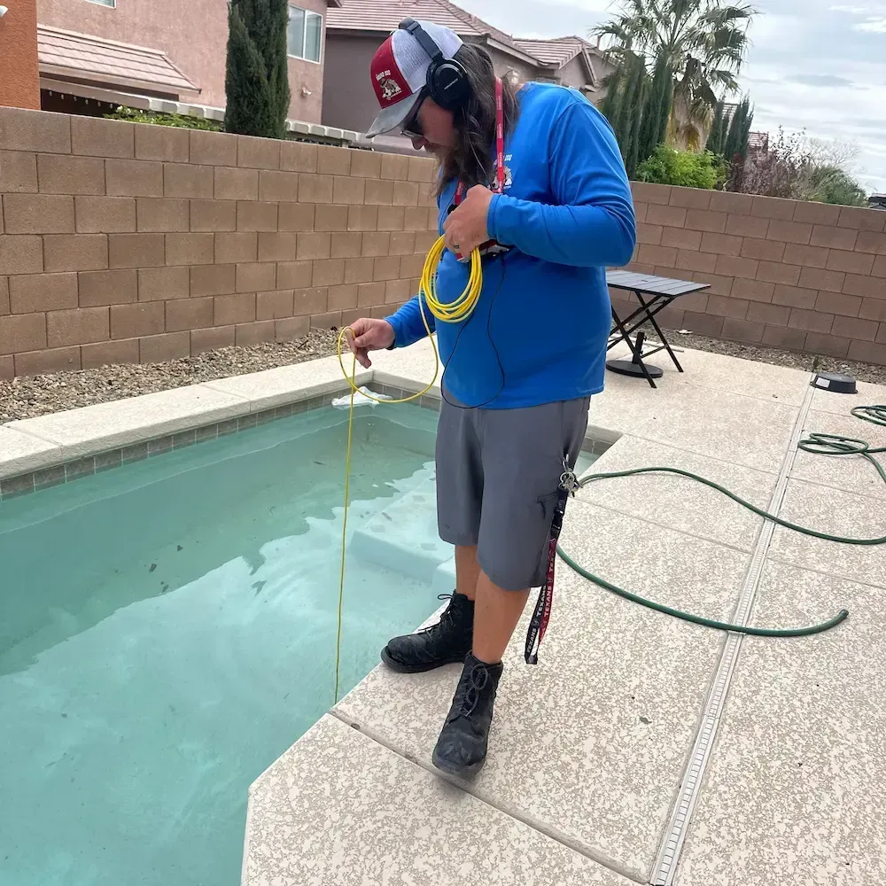 Person measuring pool water with a yellow test kit beside a backyard swimming pool