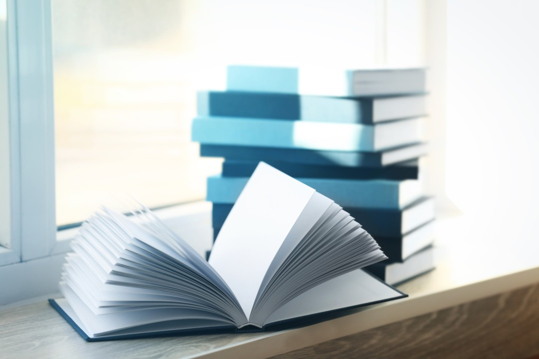 Several books and a blank open journal on a windowsill
