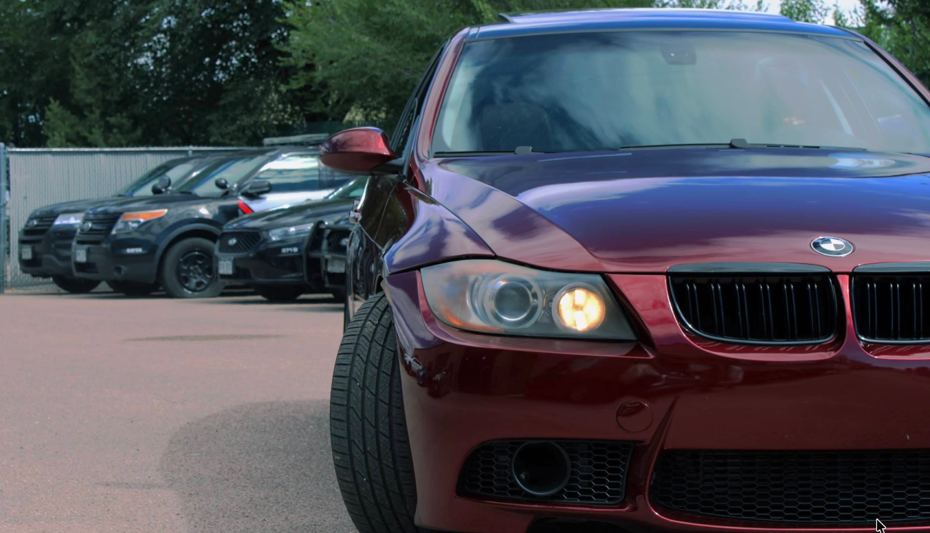 Red BMW car parked in front of two police cars. | Jeanithe Motorsports