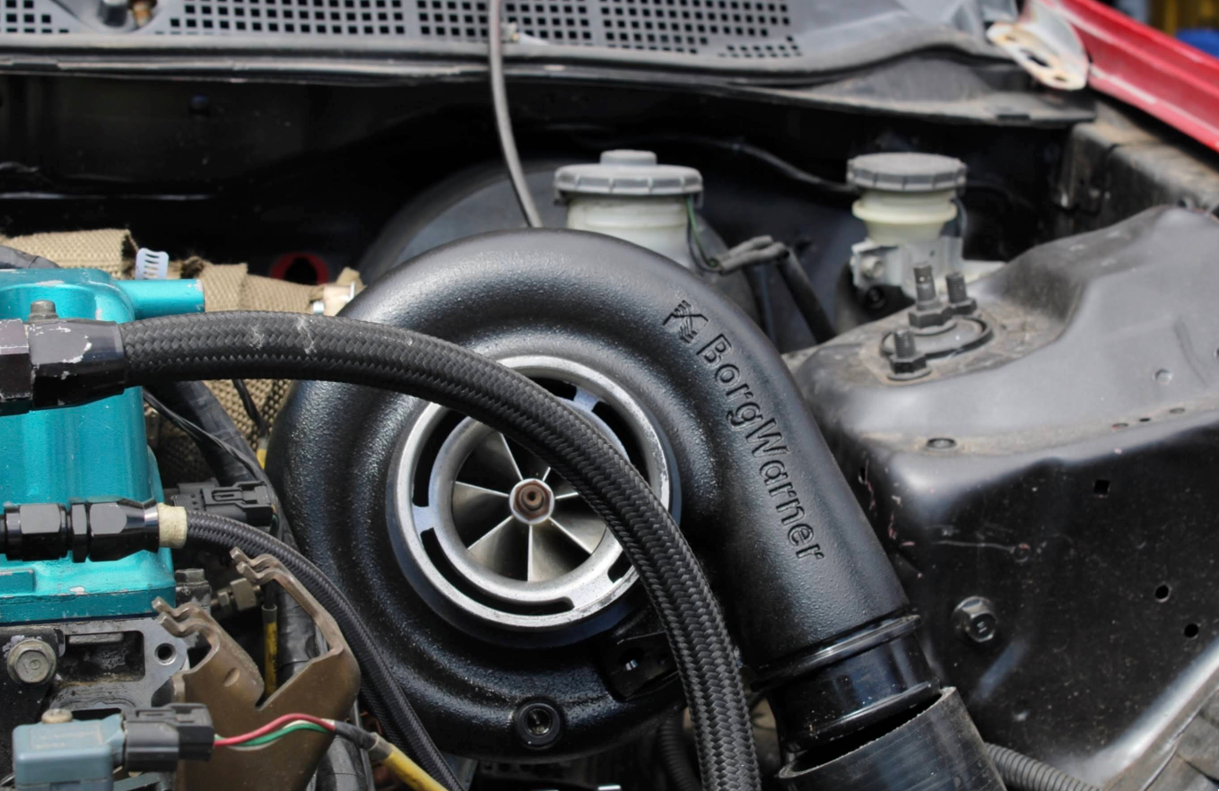 Black turbocharger installed in a car engine bay, with associated hoses and components. | Jeanithe Motorsports