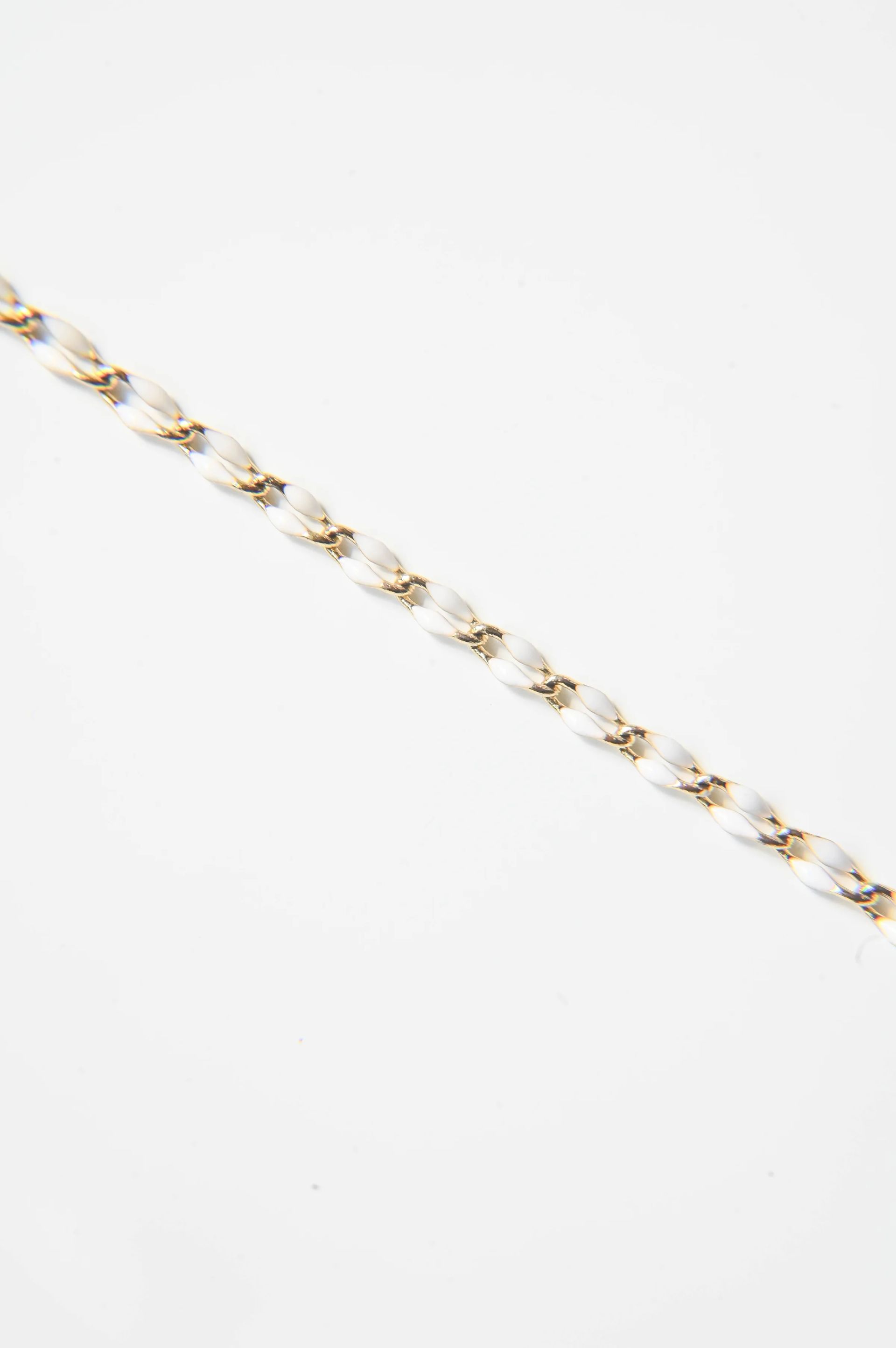 A close up of a gold chain with pearls on a white background.