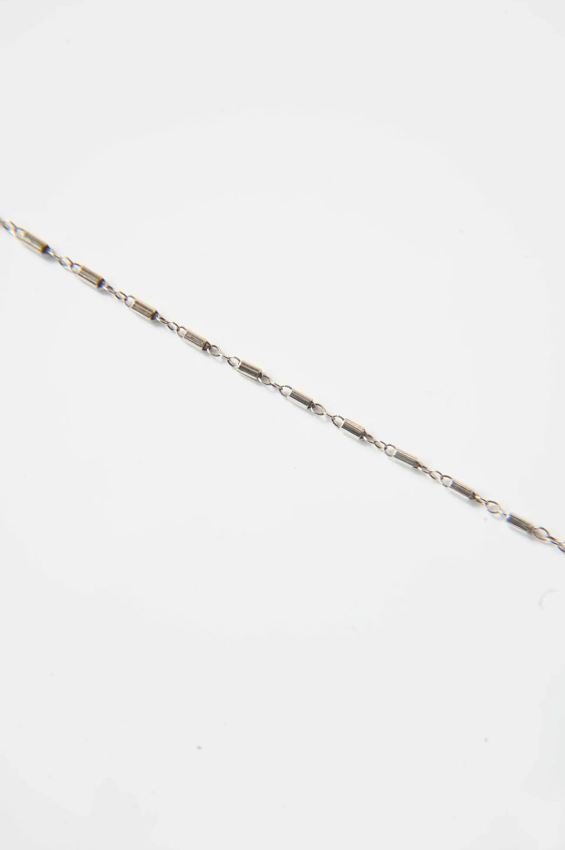 A close up of a silver chain on a white surface.