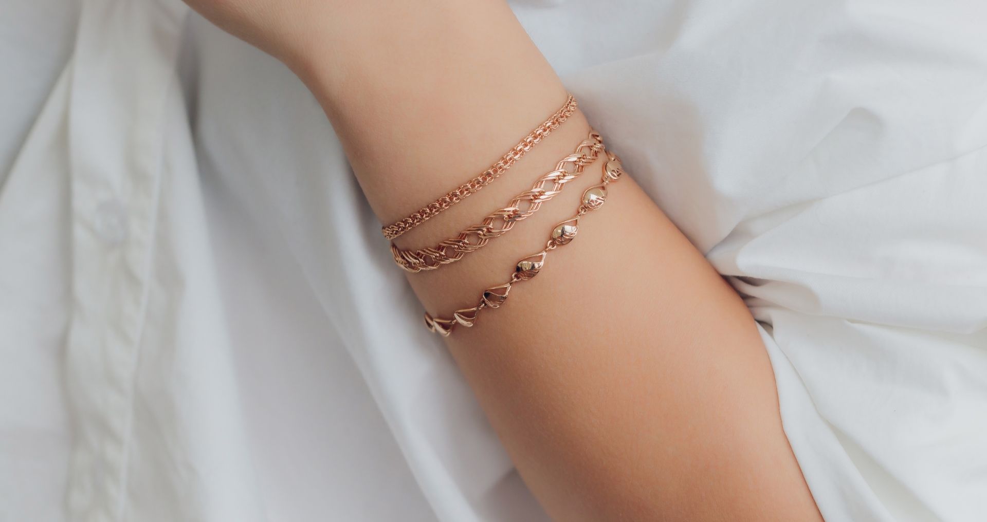Arm with three rose gold bracelets on a white shirt.