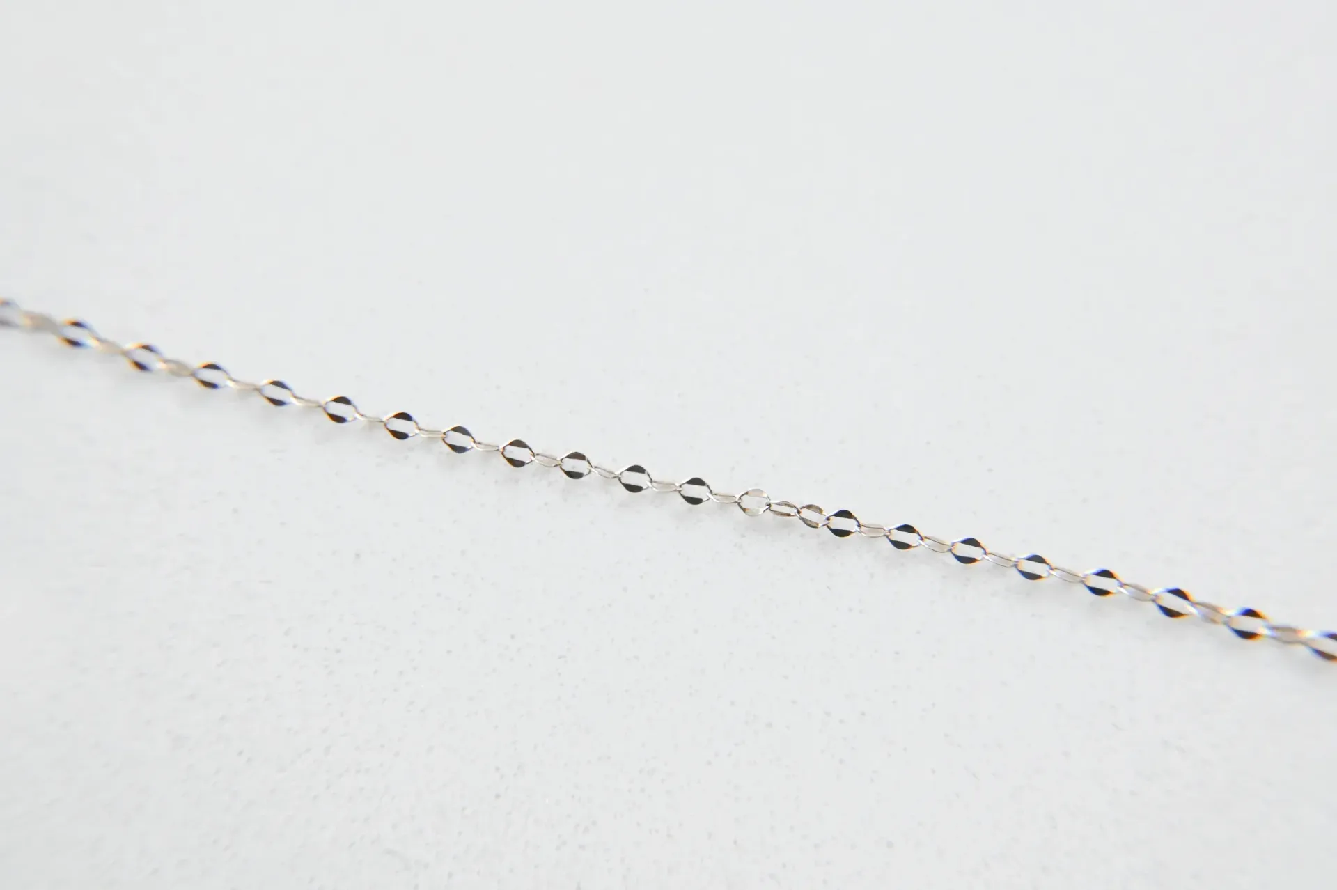 A close up of a silver chain on a white surface.