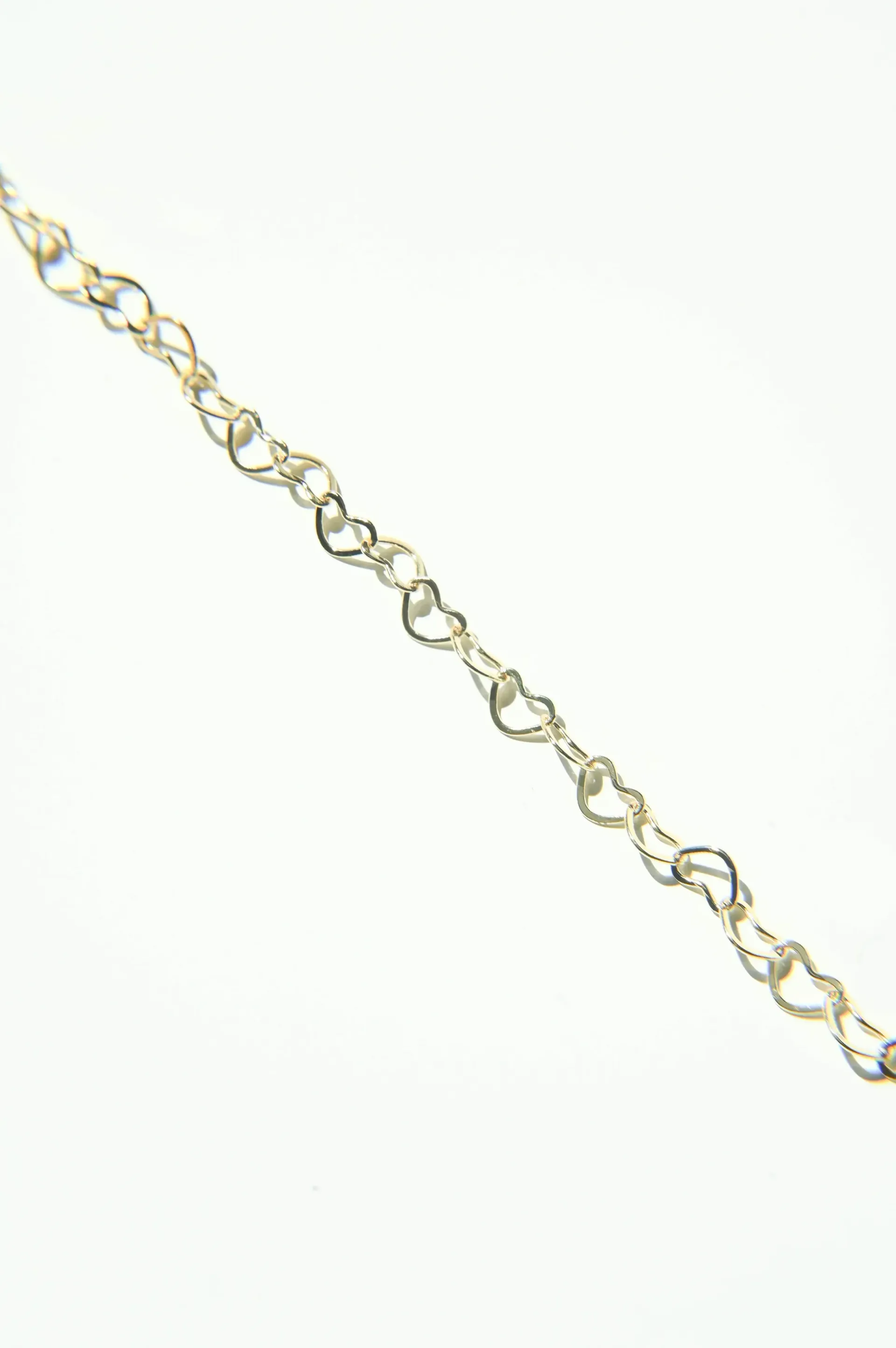 A gold chain with hearts on it on a white background.