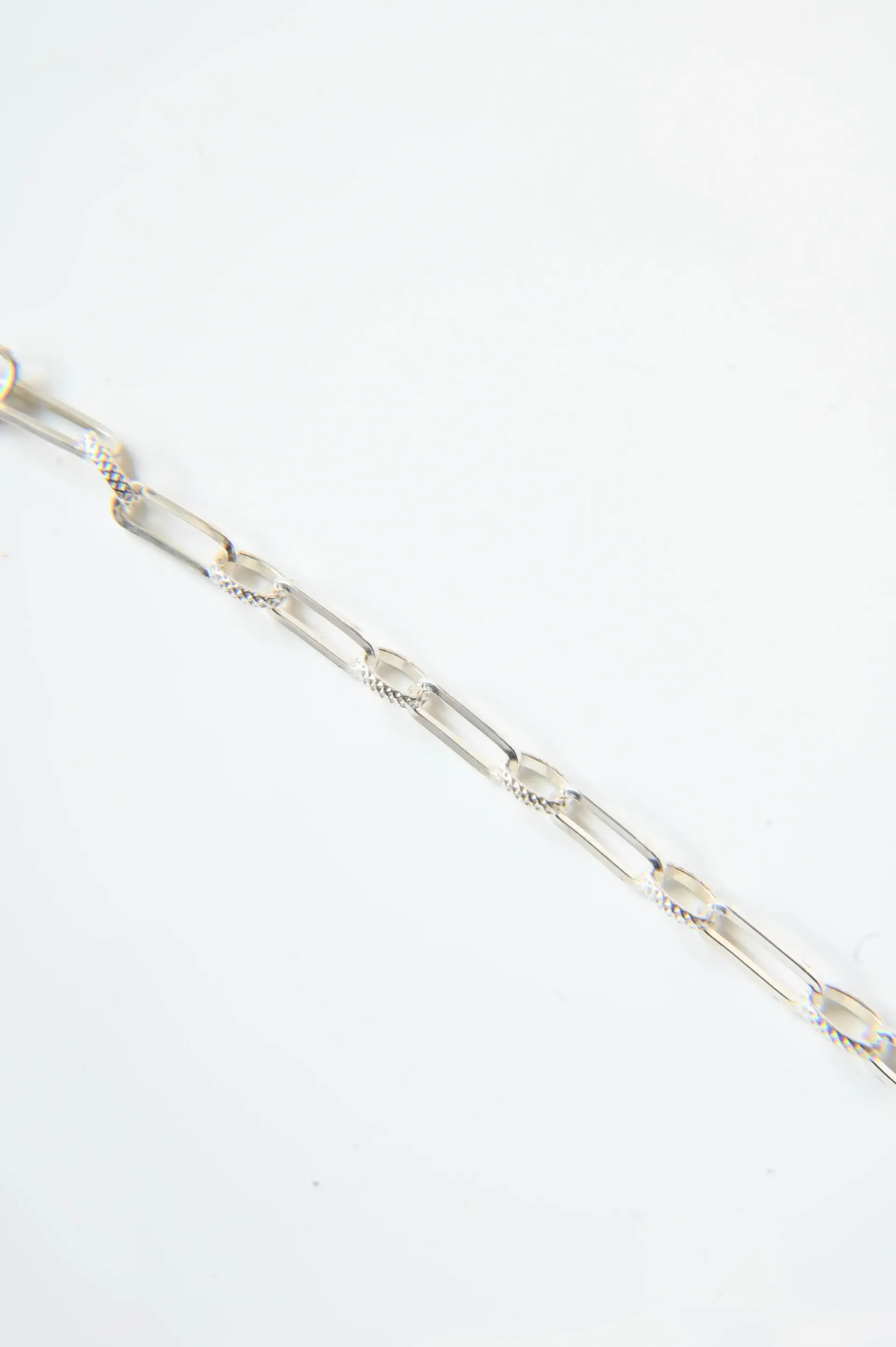 A close up of a silver chain bracelet on a white surface.