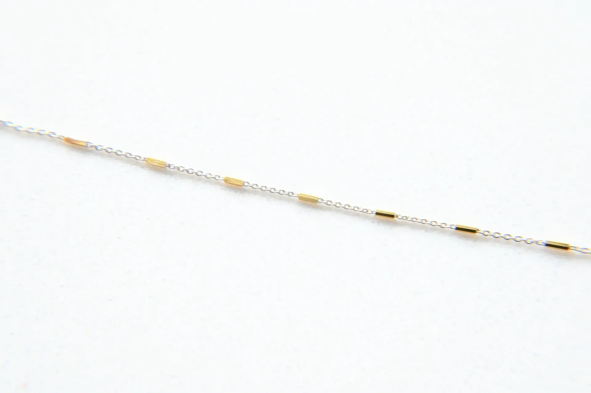 A close up of a silver and gold chain on a white background.