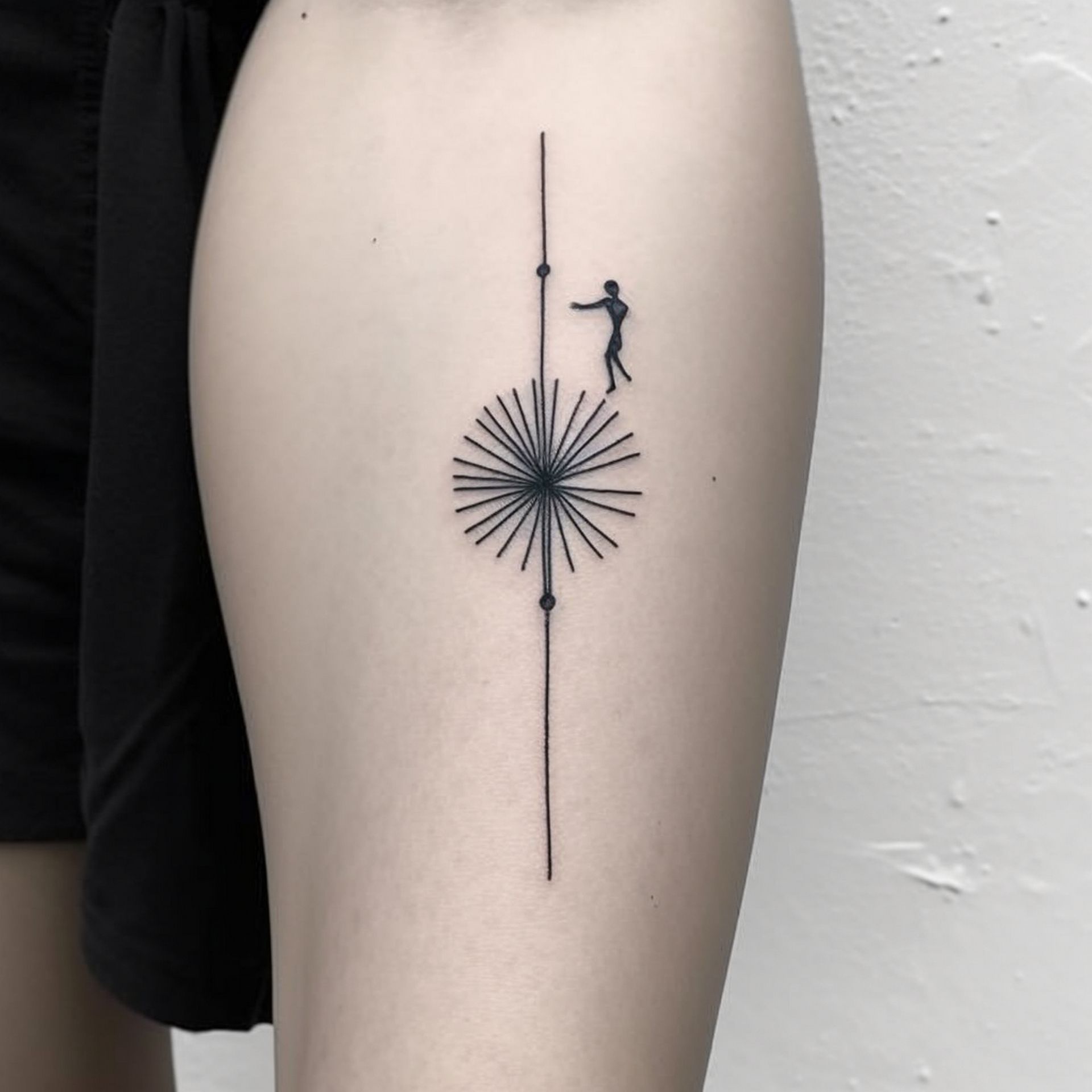 A minimalist tattoo on a person's skin featuring a thin vertical line, a central starburst, and a small silhouette figure.