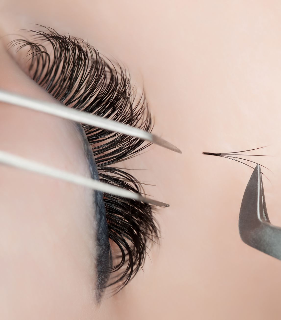 Applying eyelash extensions with tweezers on a closed eye.