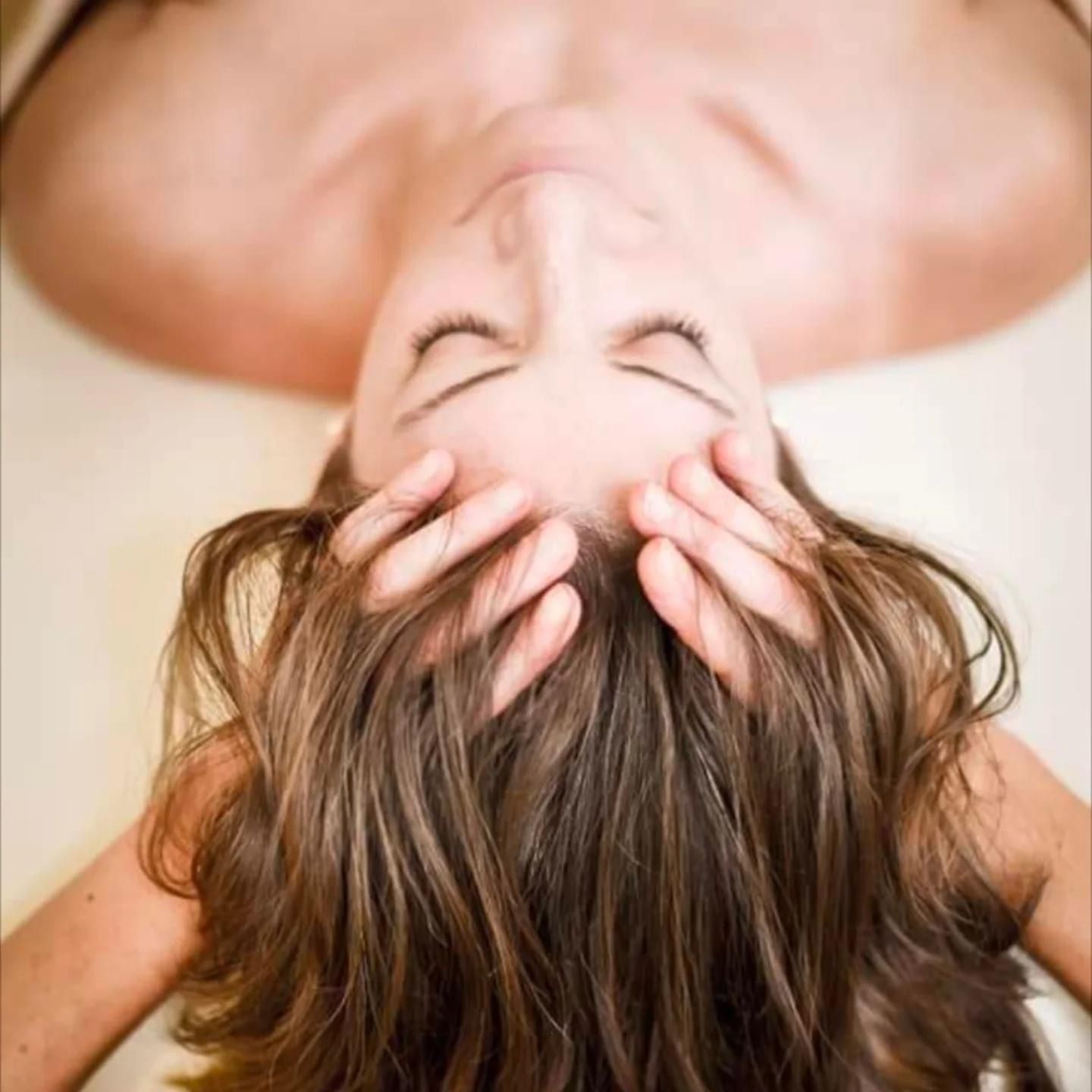 Femme recevant un massage de la tête, les yeux fermés, les cheveux écartés, les mains sur la tête.