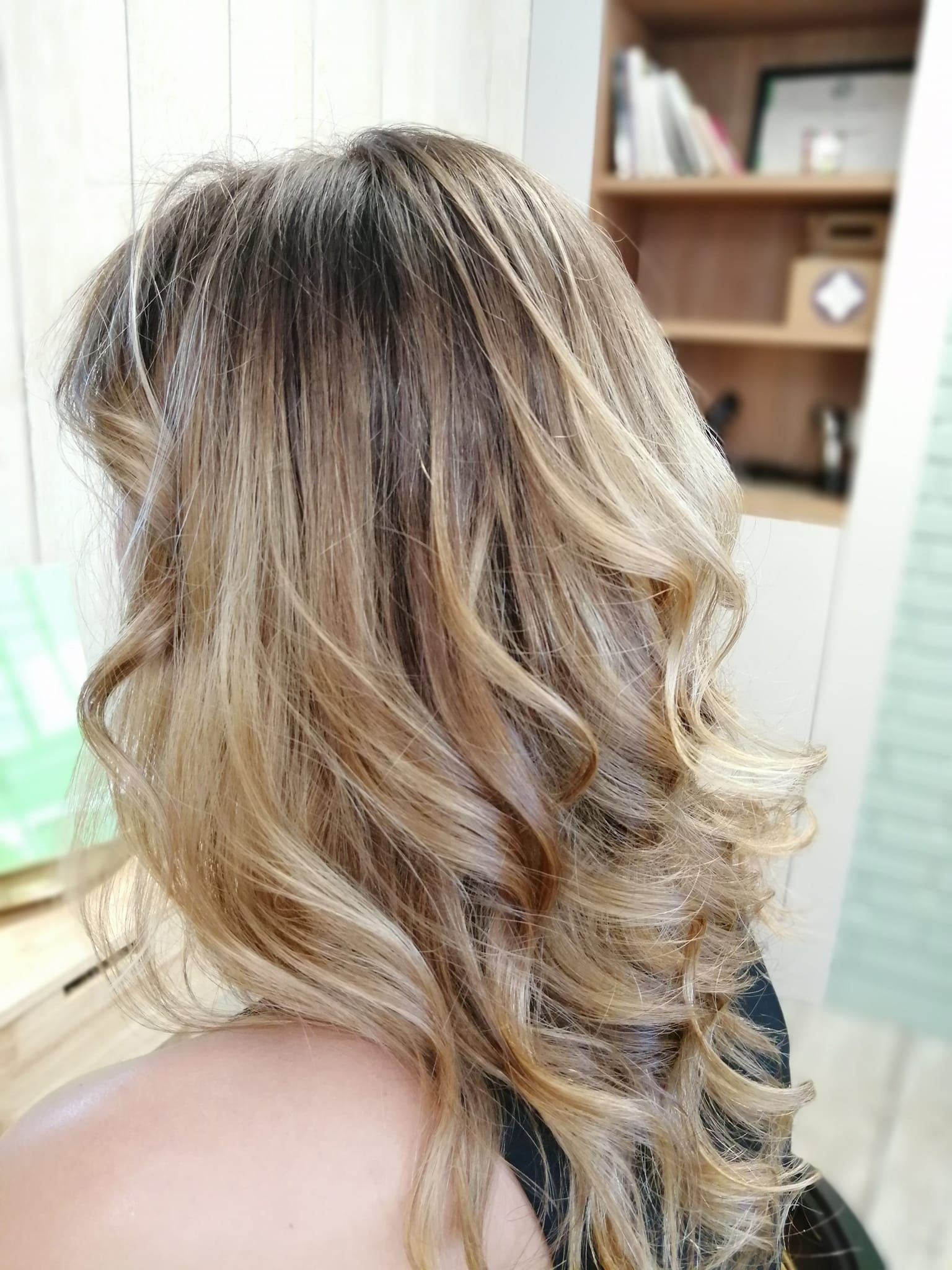 Une femme aux longs cheveux blonds est assise sur une chaise devant une étagère.