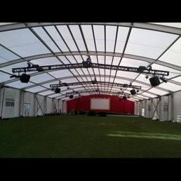 Large white tent interior with a red stage at the back and black lighting rigs suspended from the curved ceiling.
