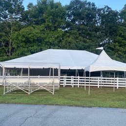 A large white tent set up on a grassy area with a white picket fence and trees in the background.
