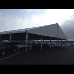 Cars parked under a large white tent in a parking lot on a cloudy day.