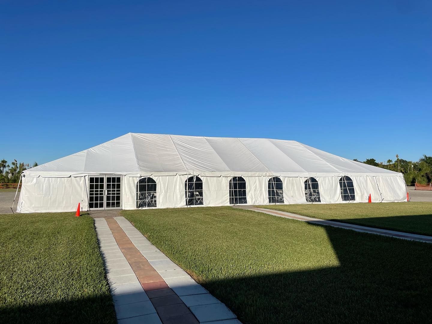 White tent on a grassy area under a clear blue sky, with a brick pathway leading to the entrance.