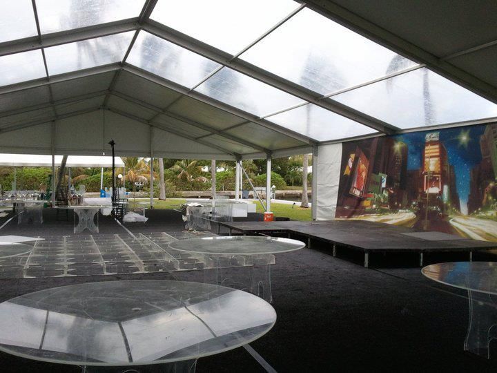 A lit dance floor in an event tent. Round tables with guests in formal attire surround the dance floor; a band performs in the background.