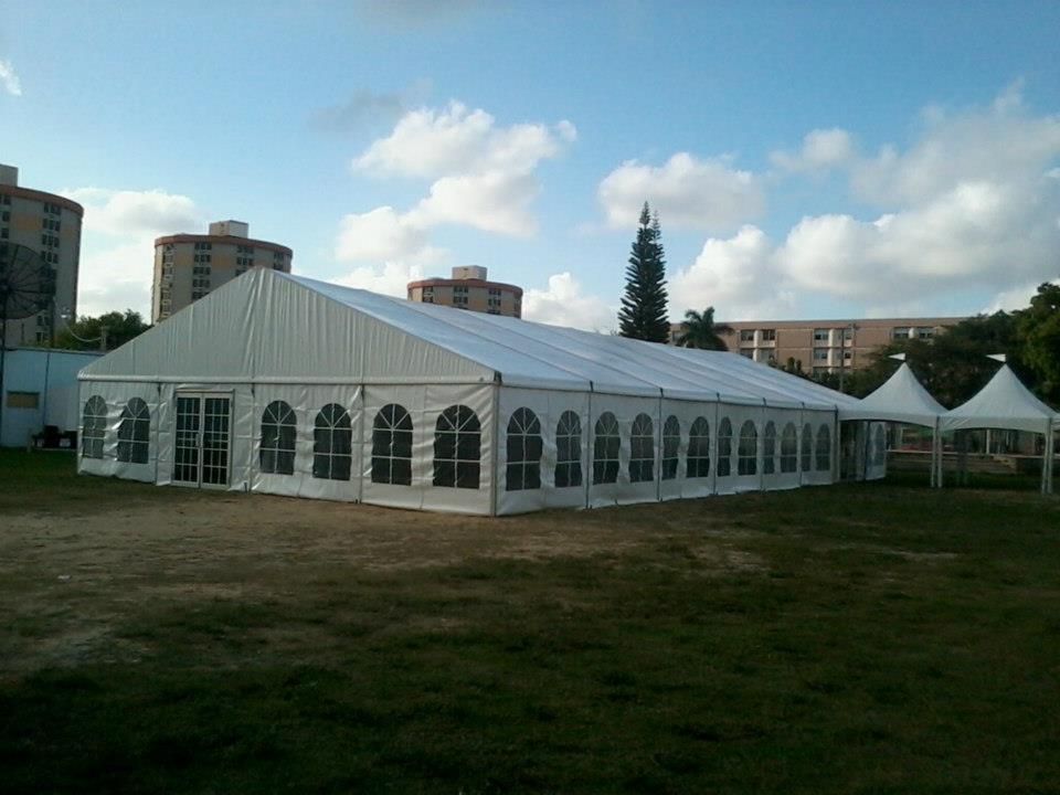 A large white tent set up on a grassy field with buildings and a blue sky in the background.