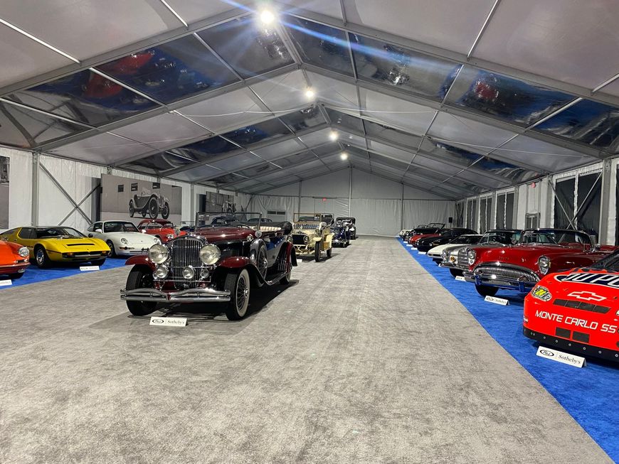 Classic cars on display inside a large tent. A vintage car is prominently in the foreground.
